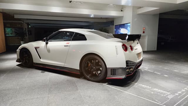 A white Nissan GTR sports car with a large rear spoiler is parked in a well-lit garage