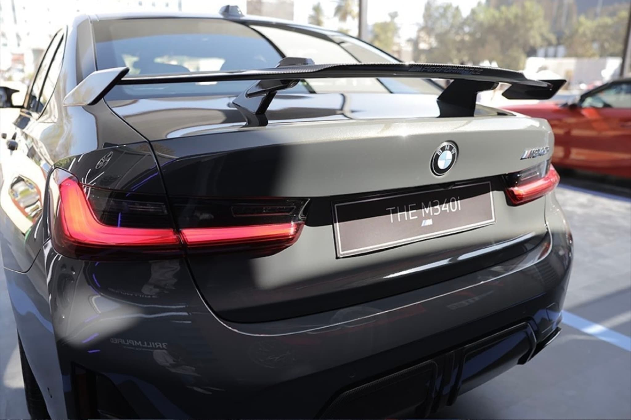 The rear view of a black BMW car with a prominent rear spoiler, illuminated taillights, and a blurred background