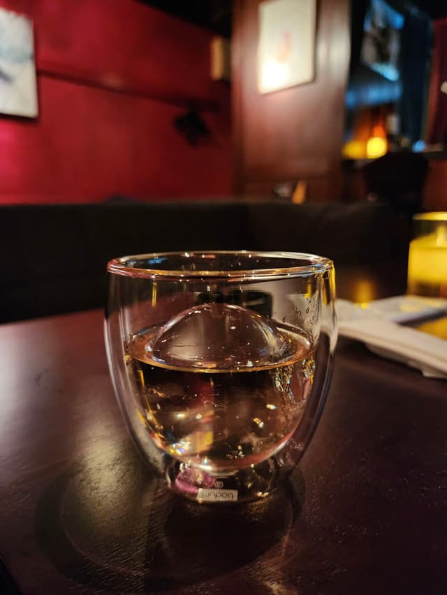 A glass of water on a dark wooden table in a dimly lit room with red walls and framed pictures