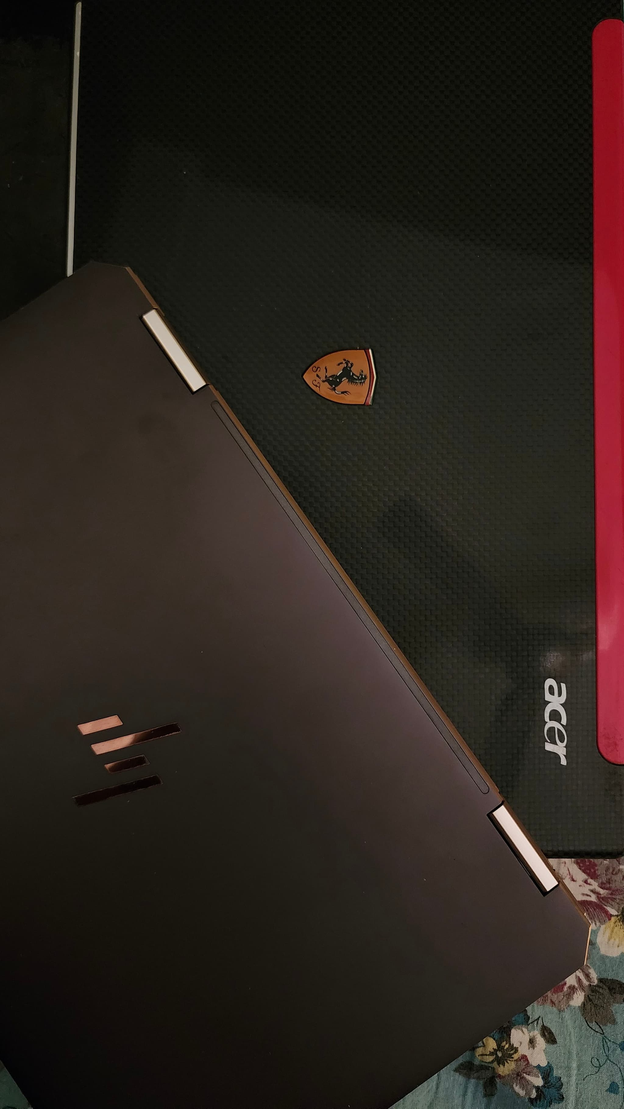 Two laptops are placed on top of each other The top laptop is an Acer, identifiable by its logo, and the bottom laptop has a Ferrari logo