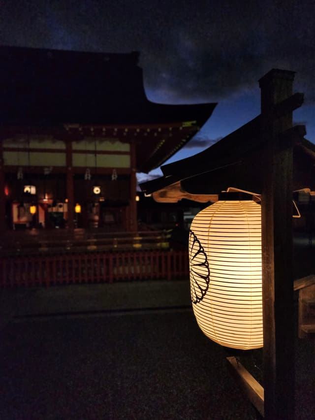 A traditional Japanese lantern illuminated at night, with a temple in the background