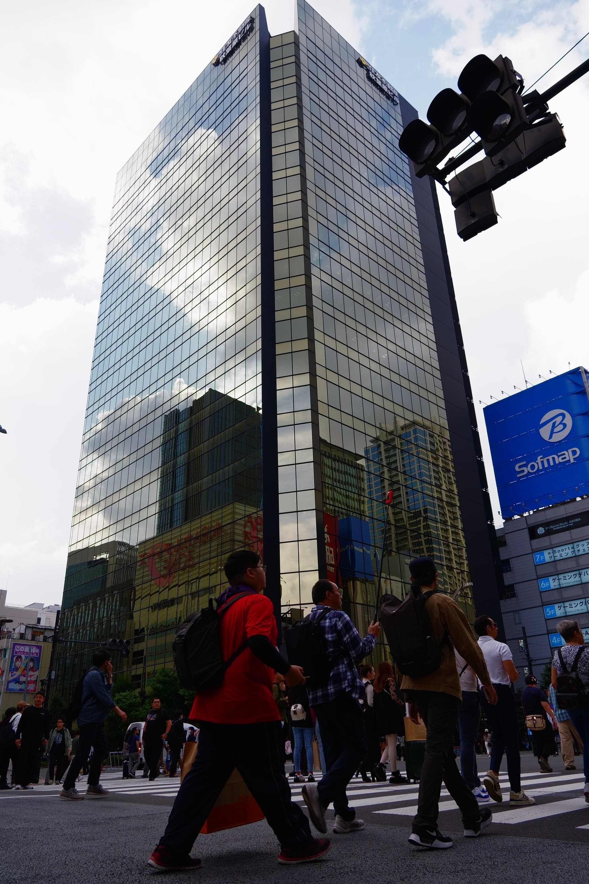 A tall, reflective glass skyscraper with people walking in the foreground and a traffic light overhead