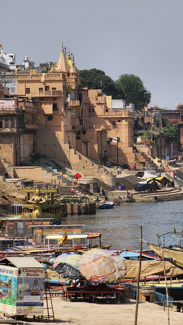 A riverside scene in Varanasi, India, featuring ancient buildings, boats, and ghats along the Ganges River The area is bustling with activity, including people and various structures