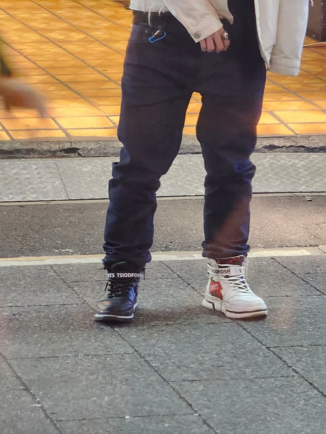 A person wearing mismatched shoes, one black and one white, standing on a tiled sidewalk