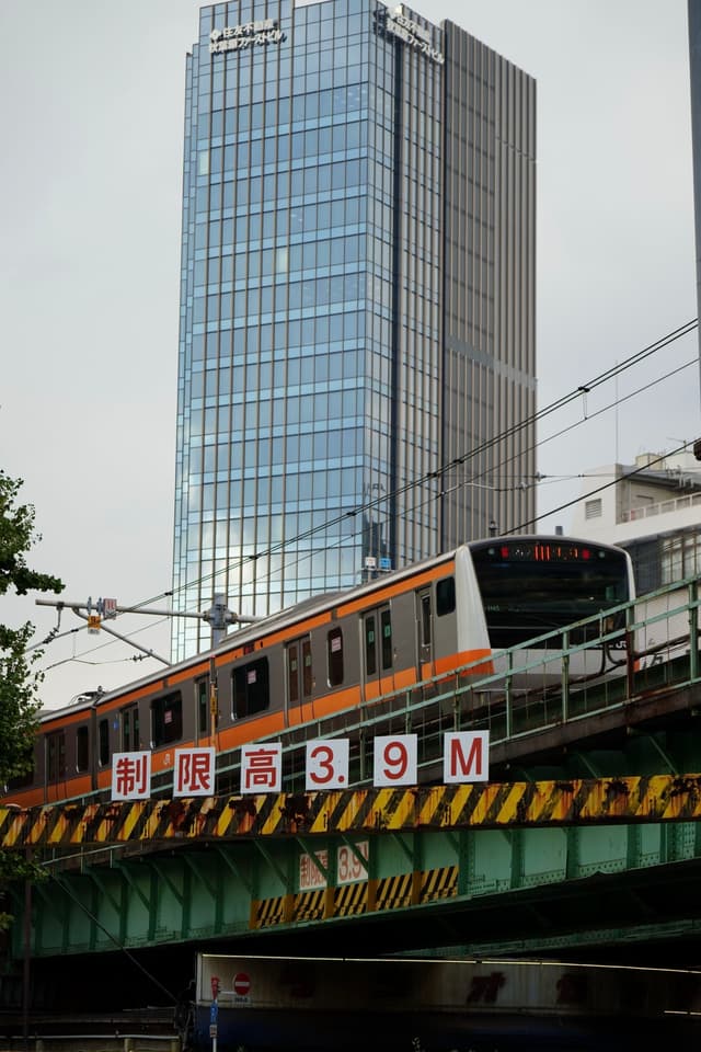 A train crossing a bridge with a height restriction sign of 39 meters, set against the backdrop of a tall, modern glass building