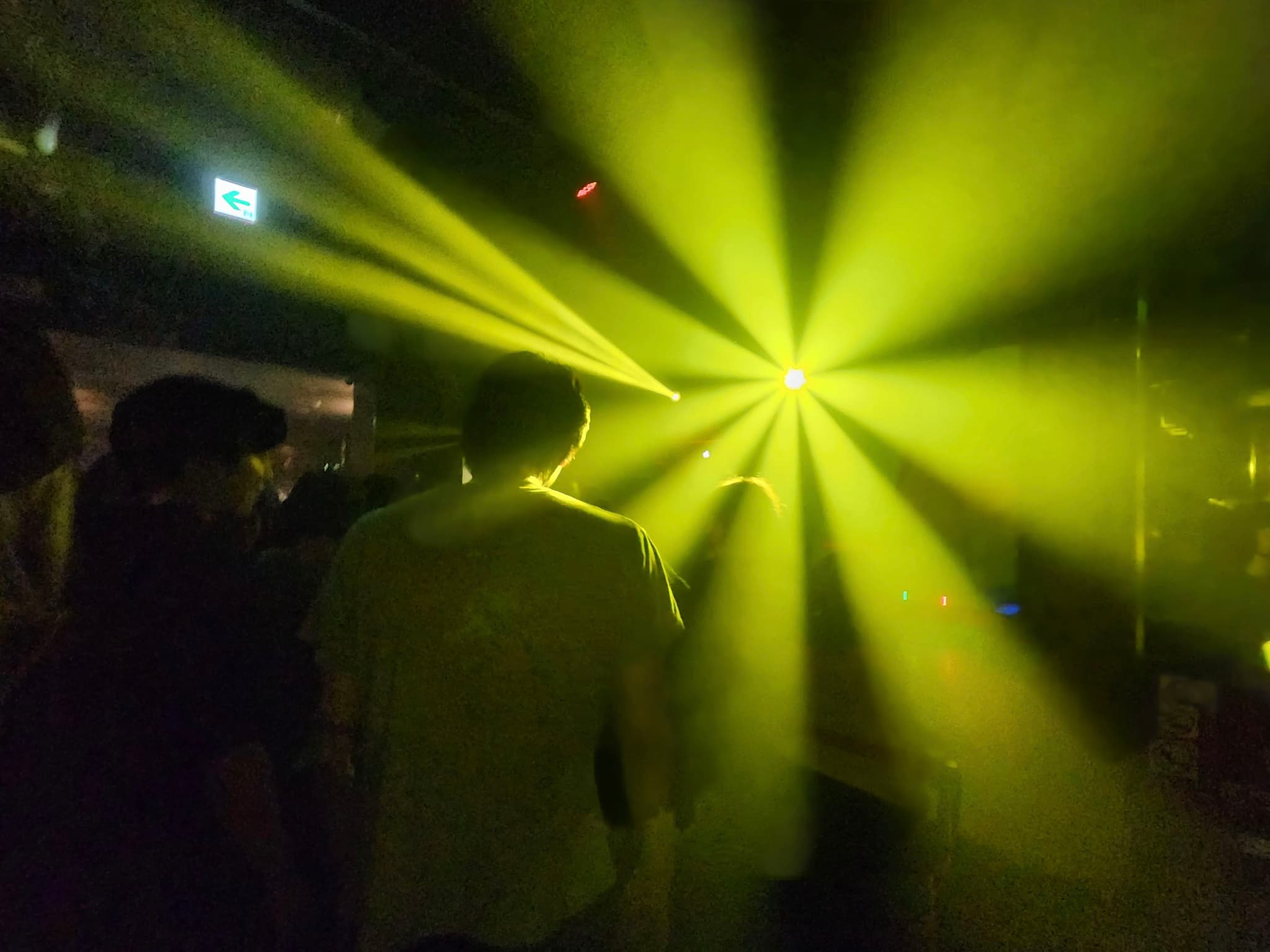 A group of people standing in a dark room with bright yellow stage lights creating a starburst effect