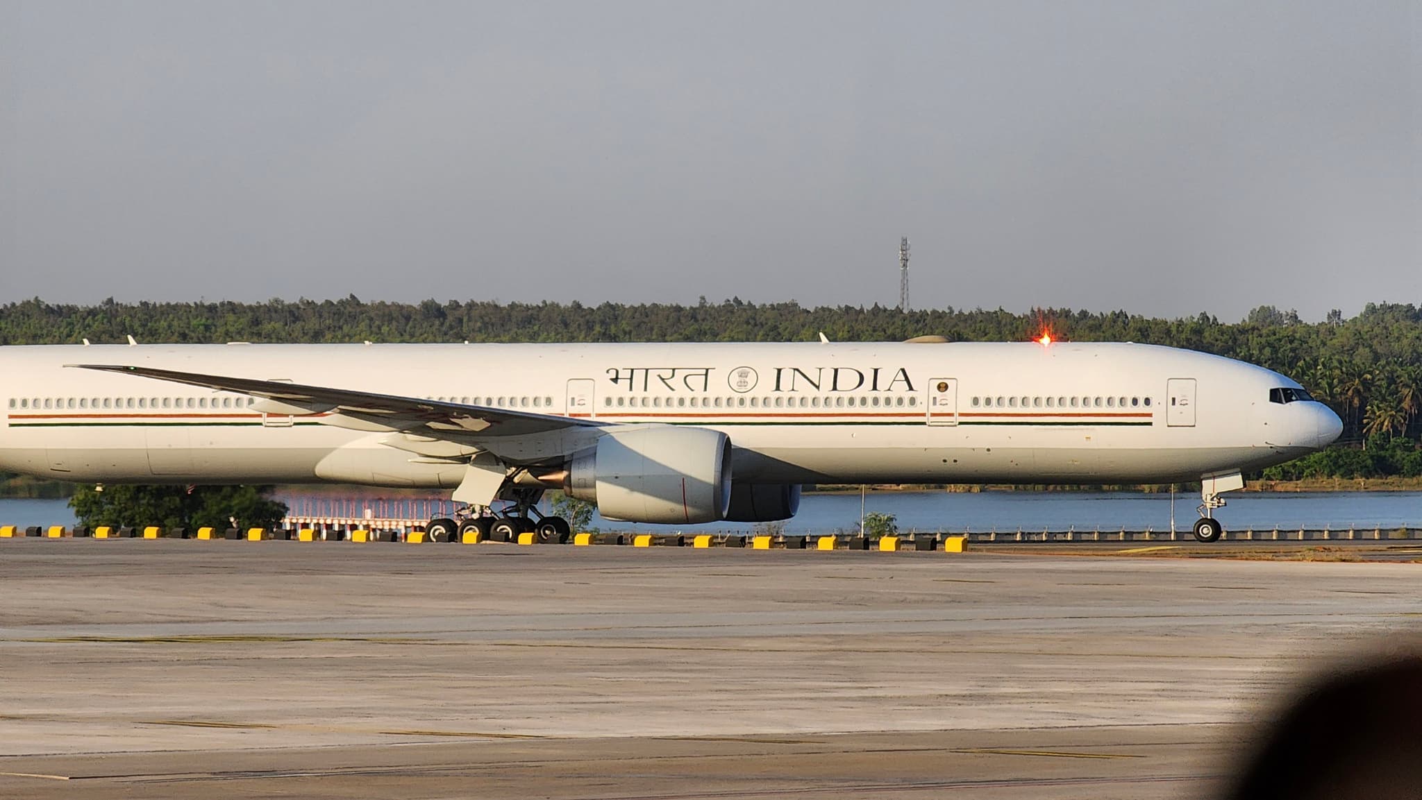 A Vistara aircraft is taxiing on a runway at an airport, with trees and a body of water visible in the background