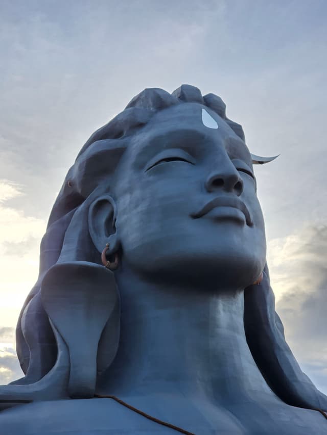 A large statue of a serene-faced figure with long hair and a prominent forehead mark, set against a cloudy sky