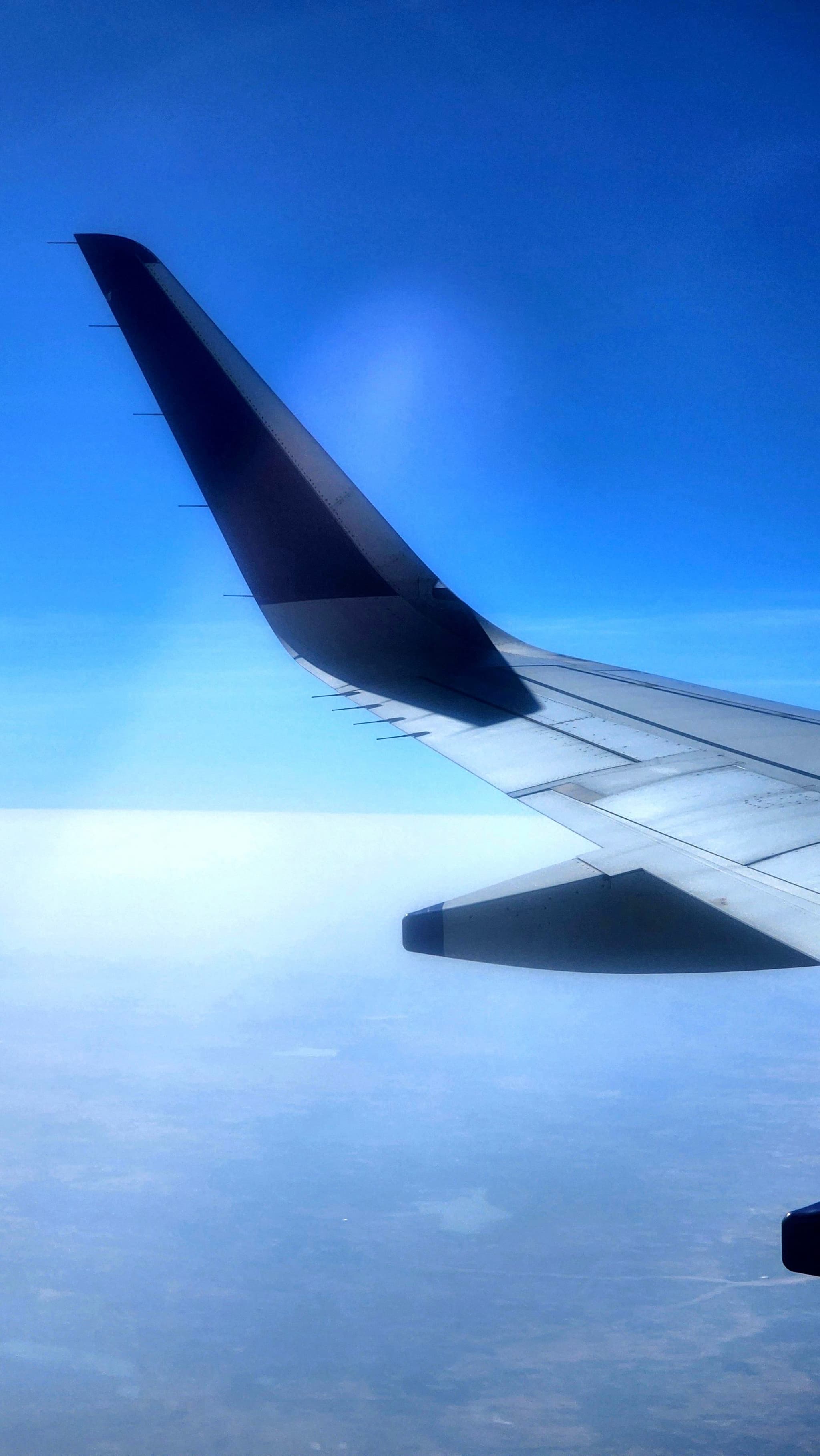 An airplane wing against a backdrop of a clear blue sky and distant landscape below