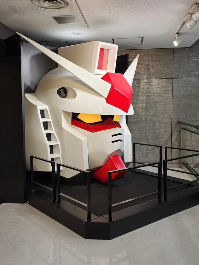 A large, detailed model of a Gundam head displayed indoors, surrounded by a black railing