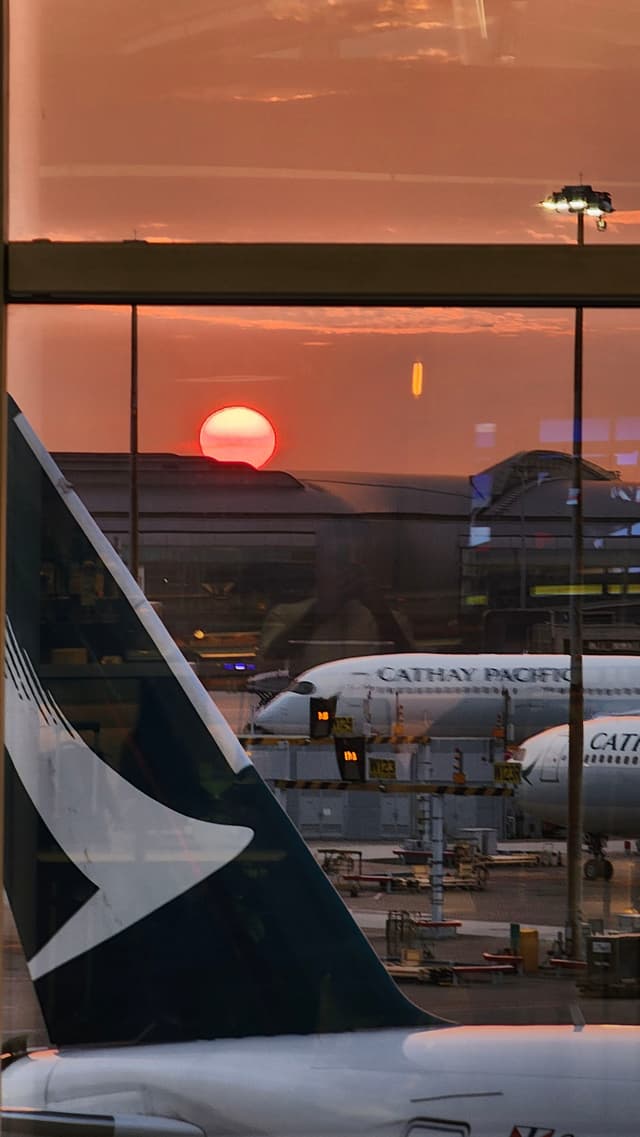 A sunset view at an airport with Cathay Pacific airplanes on the tarmac, seen through a large window