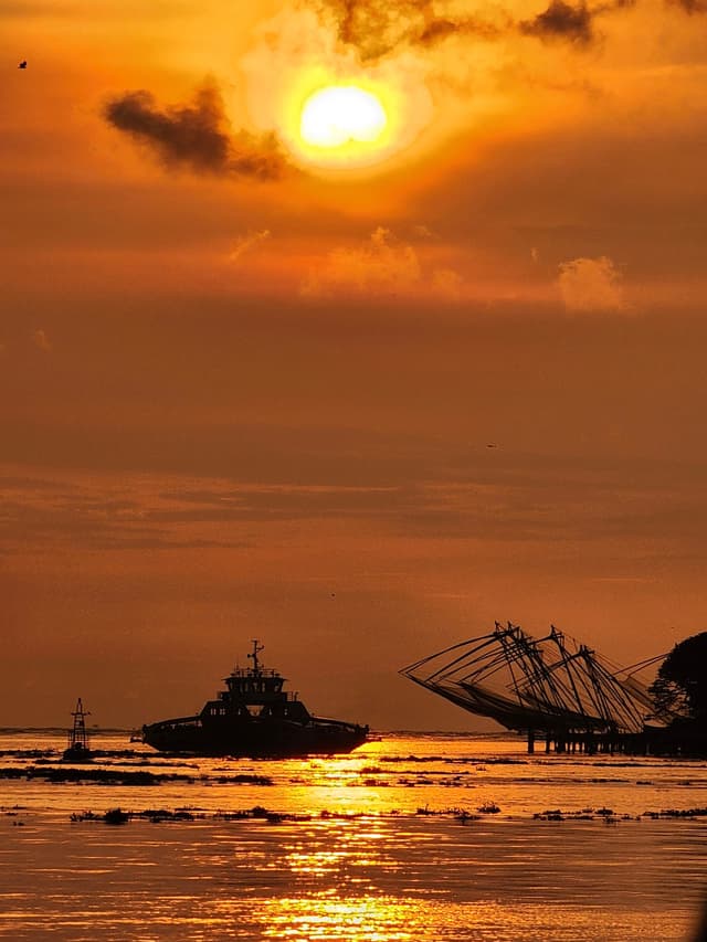 A serene sunset over the ocean with silhouettes of boats and a glowing reflection on the water